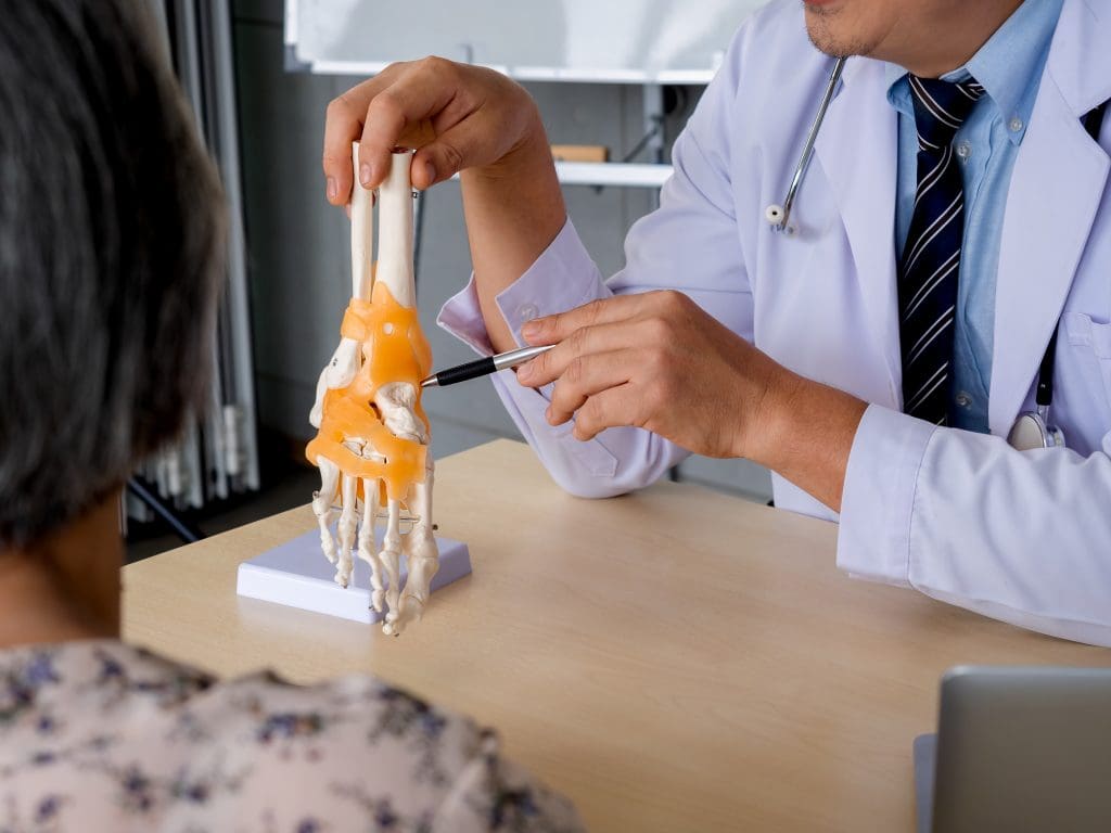 closeup pen holding by orthopedic doctor man s hand white coat pointing foot skeleton ankle joint anatomy model desk explain patient medical office physio treatment concept LIV Hospital
