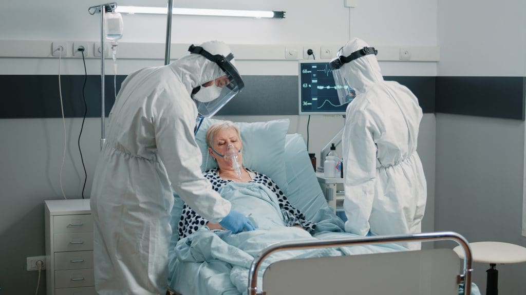 Team of paramedics in hazmat suits checking on patient healthcare. Medical staff with protection against coronavirus outbreak consulting woman with oxygen tube in quarantine isolation zone