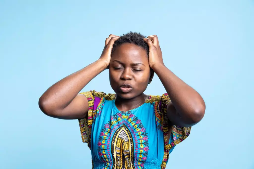 A fatigued person sits slouched in a dimly lit, cluttered room. Their expression is weary, eyes heavy-lidded. Muted colors, soft lighting from a single lamp casts shadows, creating a somber, introspective atmosphere. The figure's posture conveys the physical and mental exhaustion of brain tumor-related fatigue. The background is blurred, hazy, with indistinct shapes suggesting clutter, chaos, and the individual's struggle to focus. A sense of heaviness, malaise, and the burden of the condition permeates the scene.
