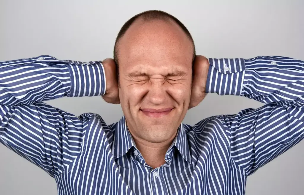 A close-up view of a human head experiencing the symptoms of a brain tumor headache. The forehead is creased with a pained expression, and the temples are slightly flushed. The eyes are squinted, and one hand is gently massaging the side of the head. The lighting is soft and diffuse, creating a moody, introspective atmosphere. The background is blurred and out of focus, placing the emphasis on the intense, agonizing headache experience. The image conveys the sense of a persistent, debilitating pain that is the primary warning sign of a brain tumor.