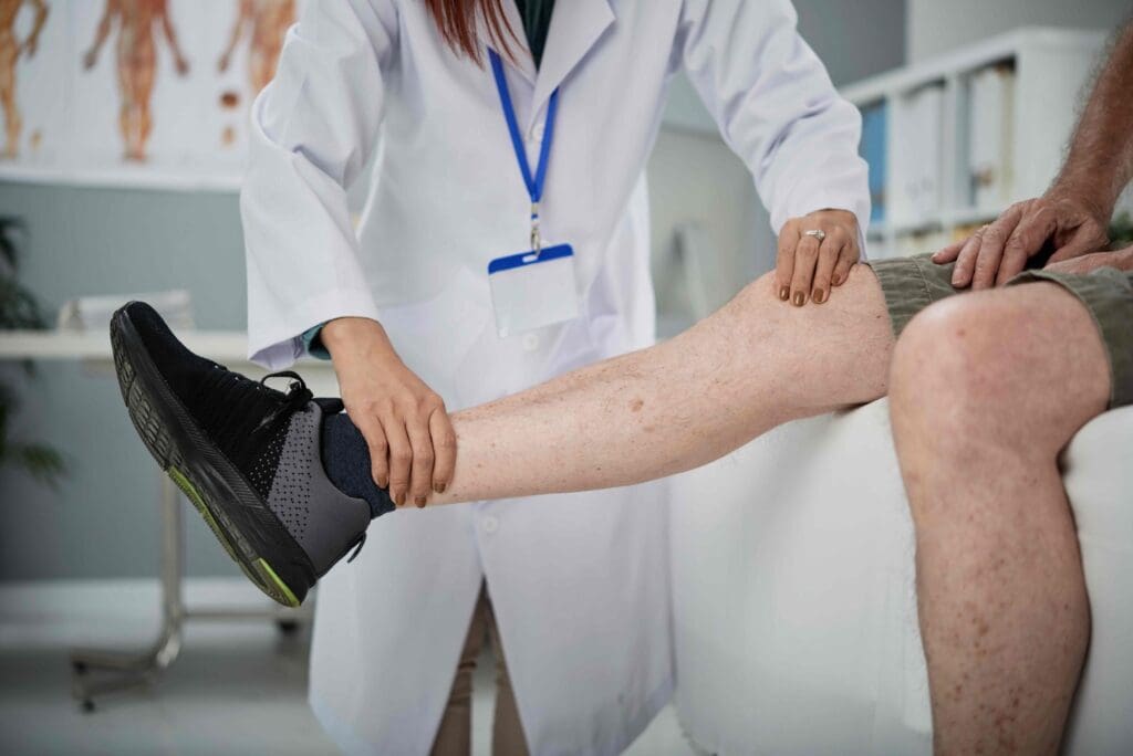 A brightly lit medical examination room, with a central focus on a person's leg extended for a close-up view of the knee joint