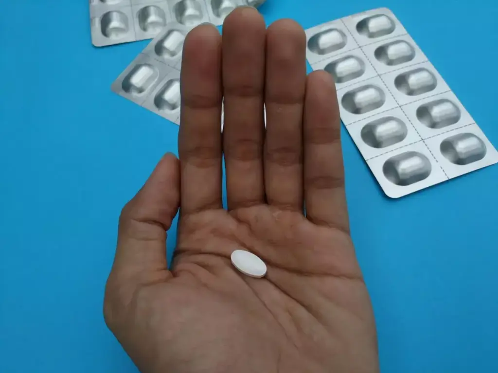 A detailed close-up of a person's hand, palm facing up, with visible veins and discoloration due to the effects of chemotherapy and steroids. The hand is surrounded by a soft, diffused light, creating a somber and introspective atmosphere. In the middle ground, various pill bottles and medical supplies are scattered, symbolizing the aftermath of the grueling cancer treatment. The background is blurred and muted, suggesting the sense of isolation and personal struggle experienced during this phase of recovery. The overall mood is one of vulnerability, resilience, and the lingering physical and emotional impact of the treatment.