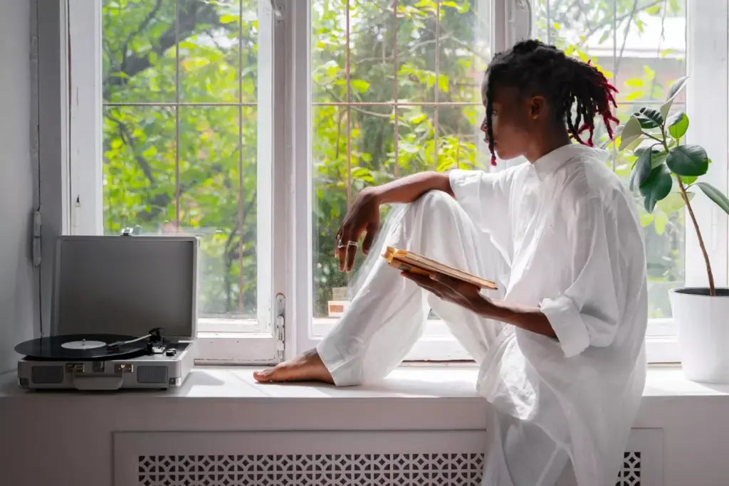 A serene and supportive environment for addiction recovery. In the foreground, a person sits peacefully, their expression one of introspection and determination. Surrounding them, a soft, warm lighting filters through a window, casting a gentle glow. In the middle ground, various self-care tools and resources are neatly arranged, symbolizing the journey of healing. The background features a tranquil, natural landscape, with trees and a calming body of water, conveying a sense of balance and connection to the world. The overall atmosphere is one of hope, resilience, and the power of inner transformation.
