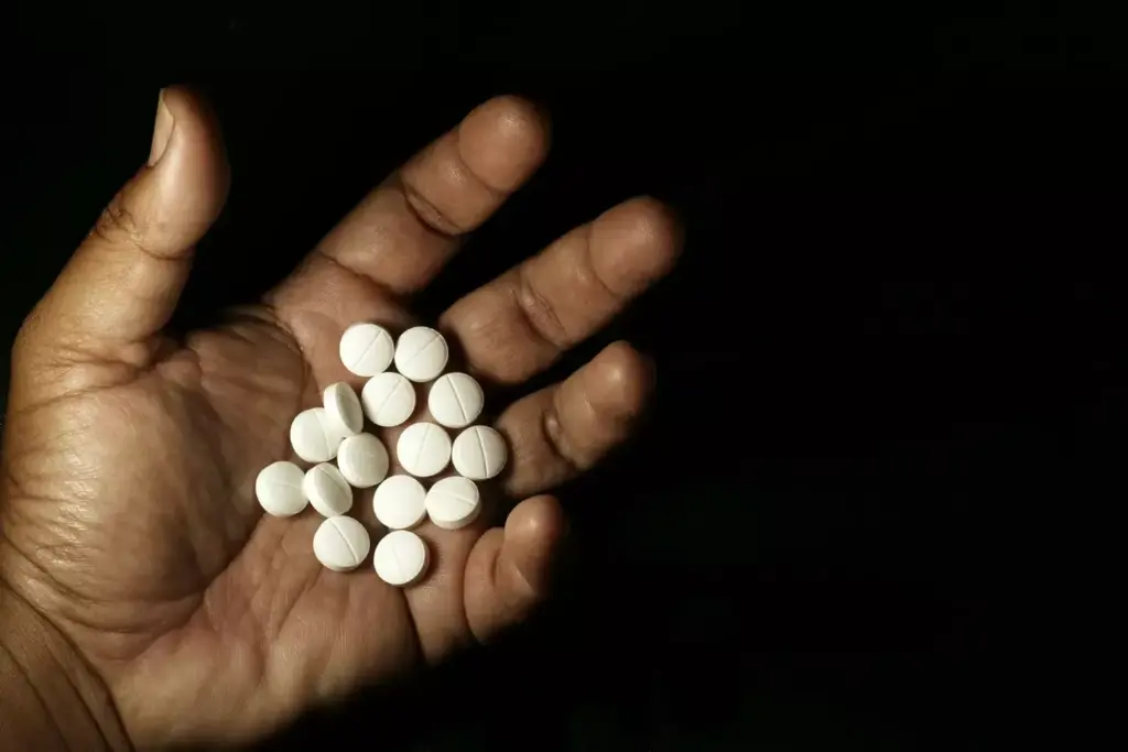 A close-up view of a woman's hand holding a small white pill bottle, against a blurred background of medical equipment and supplies. The lighting is soft and warm, creating a calming atmosphere. The pill bottle is the focal point, with a subtle depth of field effect that draws the viewer's attention to the chemotherapy medication. The overall composition suggests the personal, intimate nature of oral chemotherapy for breast cancer treatment.
