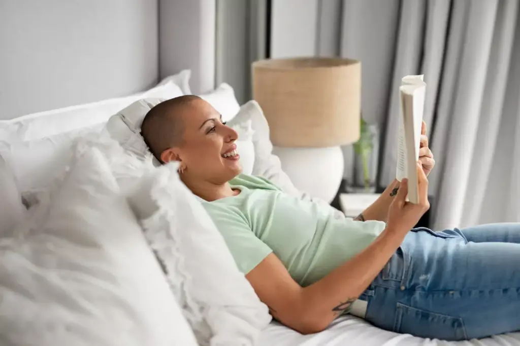A person sitting on a sofa, resting and recovering from chemotherapy. The foreground shows a person wrapped in a soft, warm blanket, their face expressing a sense of relief and tranquility. The middle ground features a glass of water and a few small personal items nearby, suggesting a cozy, comfortable environment. The background is gently blurred, with muted colors and soft lighting, creating a serene and calming atmosphere. The overall scene conveys a sense of physical and emotional healing, with the person taking time to rest and restore their energy after the challenges of cancer treatment.