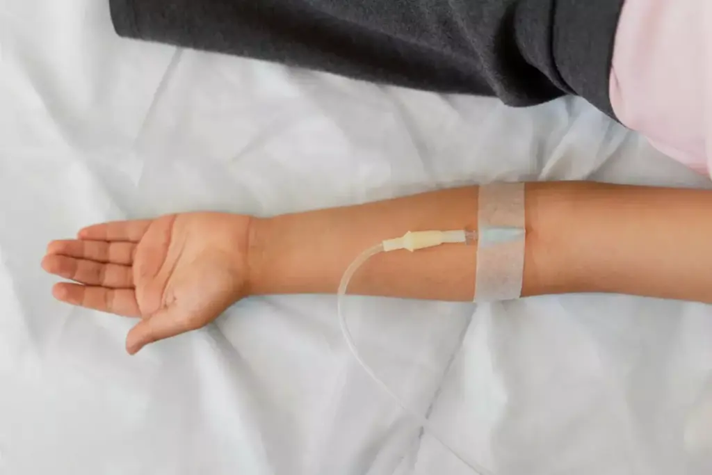 A close-up view of a woman's arm with an intravenous (IV) line delivering chemotherapy medication. The foreground shows the skin, veins, and medical tubing in vivid detail, capturing the intimate and personal nature of the treatment. The middle ground features a blurred background of a hospital room, with subtle lighting casting a warm, calming glow. The overall mood is one of quiet determination, reflecting the courage and resilience required to undergo this important stage of breast cancer management.