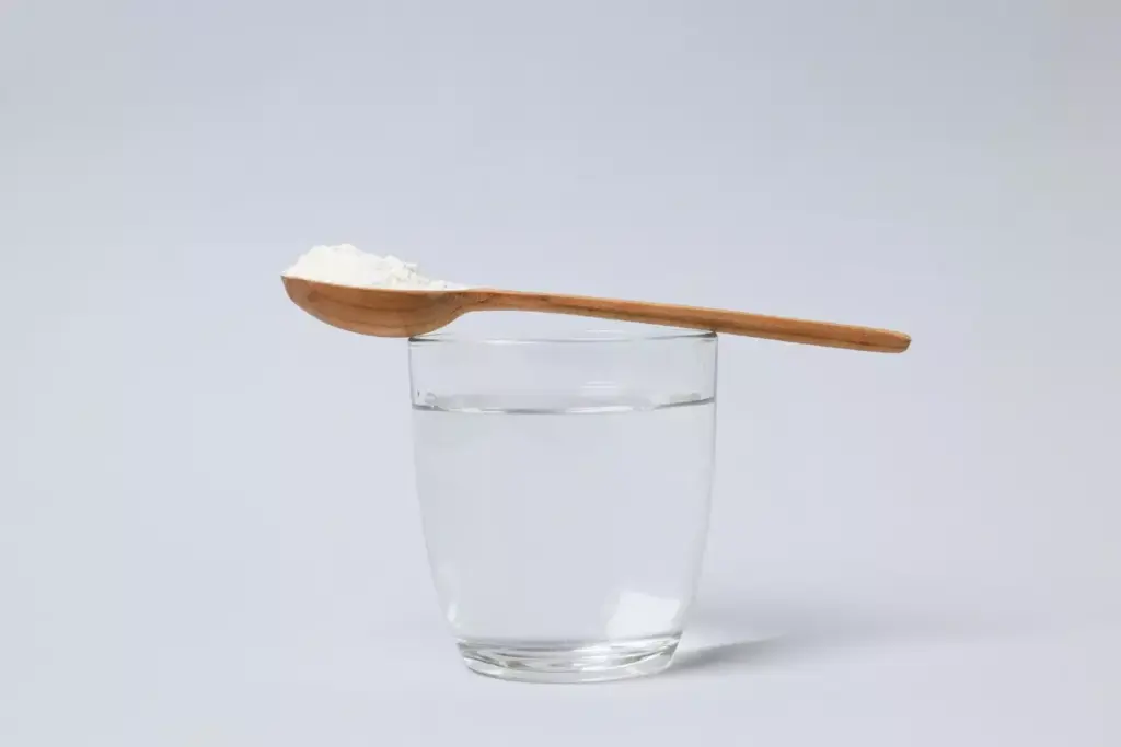 A glass filled with a clear saltwater solution, steam rising gently, placed on a simple wooden surface. In the foreground, a spoon and a small pile of baking soda. Soft, natural lighting casts a soothing, homely atmosphere. The composition emphasizes the simplicity and practicality of this time-honored remedy for chemo-induced sore throat, inviting the viewer to envision the restorative, comforting ritual of gently rinsing the mouth and throat.
