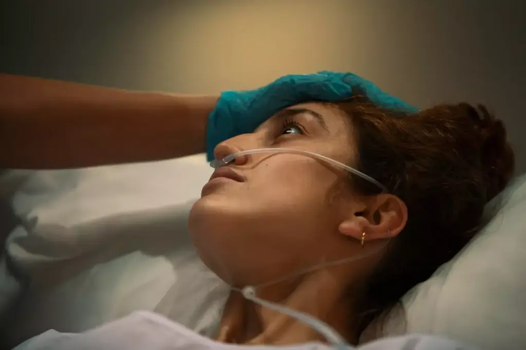 A person experiencing chemotherapy side effects, depicted in a realistic, detailed medical illustration. The foreground shows the person's face with flushed, distressed features, dry lips, and sunken eyes. The middle ground reveals the person's head with thinning, patchy hair. The background depicts a sterile, clinical setting with medical equipment and supplies, conveying the hospital environment. The lighting is soft and subdued, creating a somber, contemplative atmosphere. The overall scene captures the immediate physical and emotional toll of chemotherapy treatment.