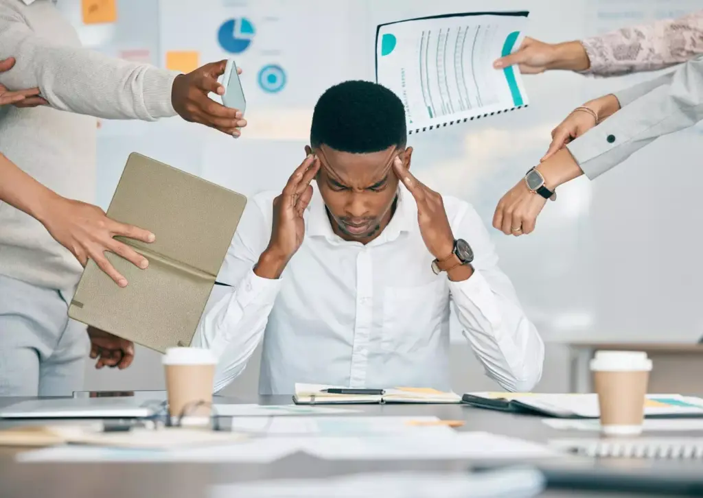 A person sitting at a desk, staring pensively at their hands, with a worried expression on their face. The desk is cluttered with various objects, suggesting distraction and disorganization. The lighting is soft and muted, creating an atmosphere of introspection. In the background, there are blurred shelves or cabinets, hinting at a professional or work-related setting. The overall mood conveys a sense of recognition of a problem or the need for help to address an underlying issue.