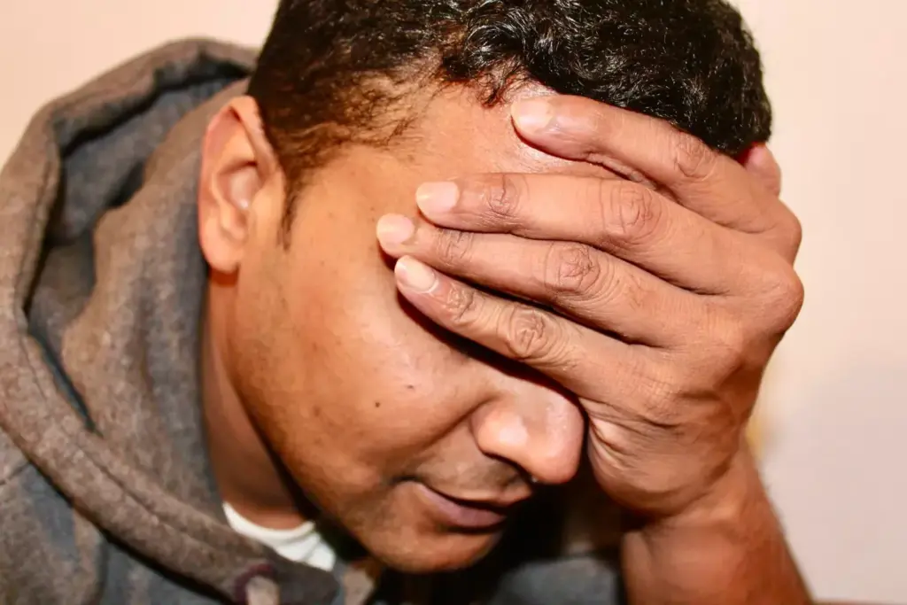 A close-up view of a person's head with a pained expression, showing the effects of chemotherapy-induced headache. The forehead is creased, and the temples are clenched, conveying the intense discomfort. The skin appears slightly flushed, with a subtle sheen of perspiration, reflecting the physiological response to the headache. The lighting is soft and diffused, creating a somber and introspective mood. The background is blurred, placing the focus entirely on the subject's face and the visible symptoms of the condition.