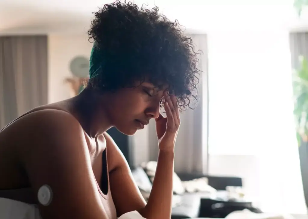 A woman experiences a chemotherapy-induced headache, her face etched with discomfort. Soft, diffused lighting illuminates her expression, casting shadows that accentuate the tension in her brow and the weariness in her eyes. The background is hazy, blurred, and muted, keeping the focus on the subject's pained countenance. The composition is tight, capturing the intimate, personal nature of the moment, conveying the physiological and emotional distress associated with the side effects of cancer treatment.