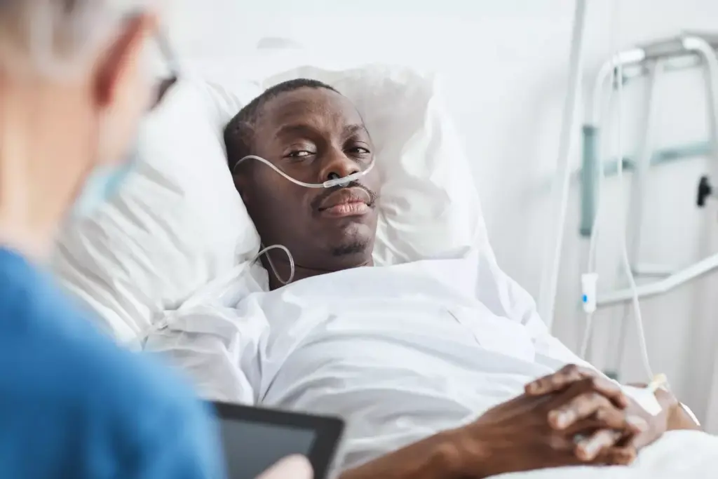  african-american man lying in hospital bed and looking at docto