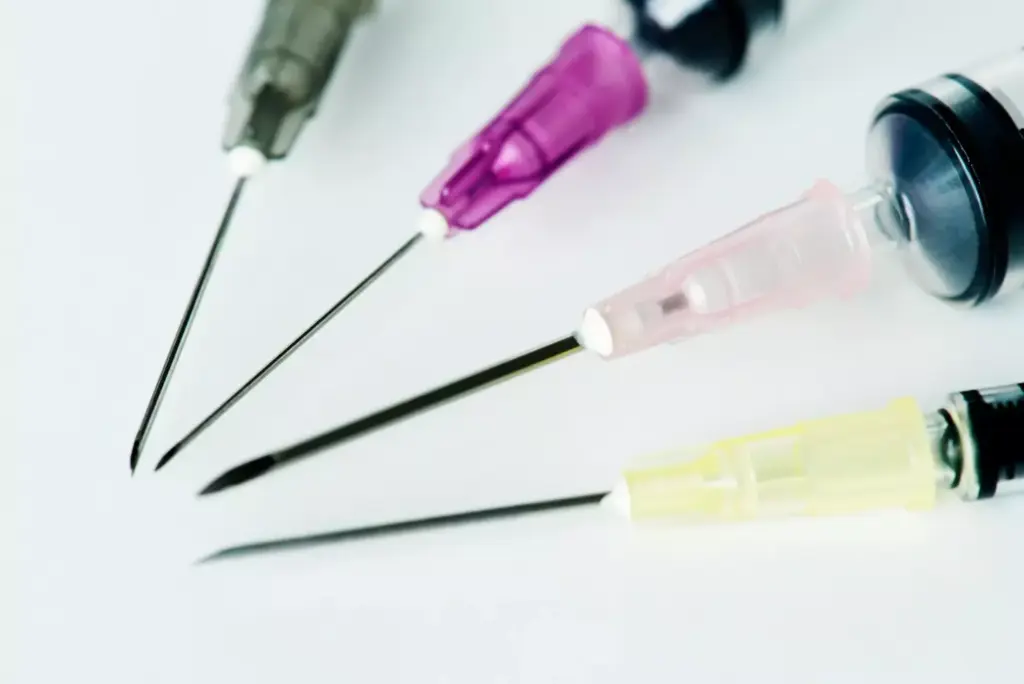 A close-up view of a selection of oncology needles, precisely arranged on a sterile medical tray. The needles are of various sizes and gauges, gleaming under bright, directional lighting that casts dramatic shadows, highlighting their sharp, precise forms. The background is blurred, creating a sense of clinical focus on the instruments. The image conveys a sense of medical expertise and the importance of carefully selecting the appropriate needle for specific cancer treatment procedures, such as chemotherapy administration or bone biopsy for metastasis diagnosis.