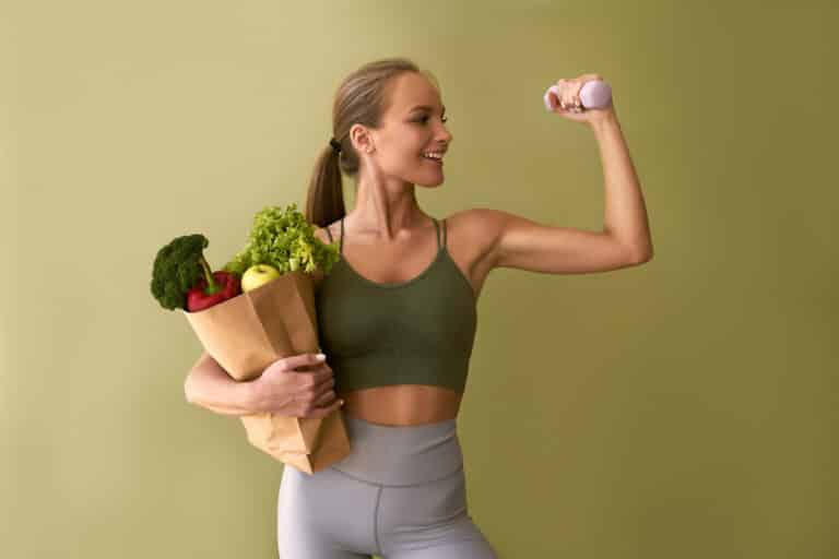 sporty beautiful woman holding bag vegetables dumbbell green background concept sports healthy eating LIV Hospital