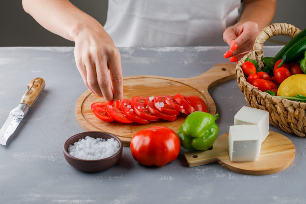 high angle view woman adding salt sliced tomatoes cutting board with knife cheese green pepper salt gray surface LIV Hospital